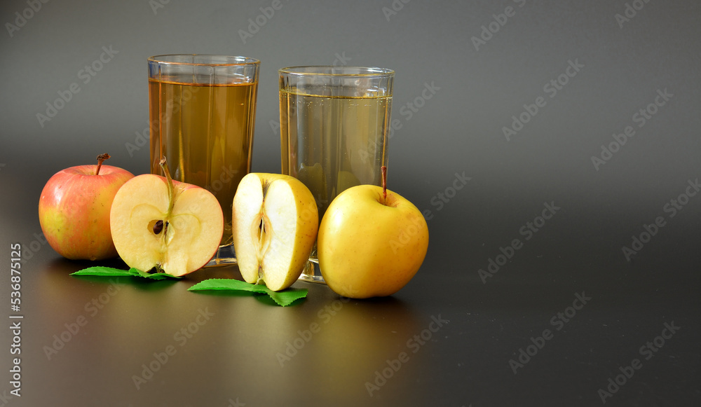 Two tall glasses with a fruit drain on a black background, next to pieces of ripe apples.