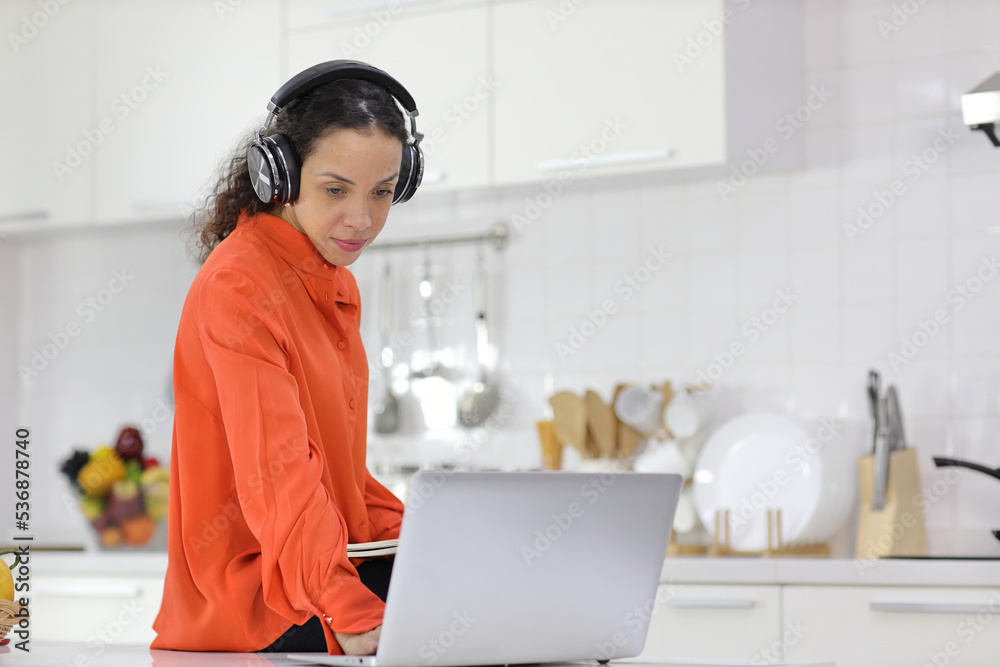 Happy latin woman learn cooking food while checking recipe from internet with computer in kitchen. Young female with headphone prepare delicious meal and listen music. Healthy and lifestyle concept Happy latin woman learn cooking food while checking recipe from internet with computer in kitchen. Young female with headphone prepare delicious meal and listen music. Healthy and lifestyle concept