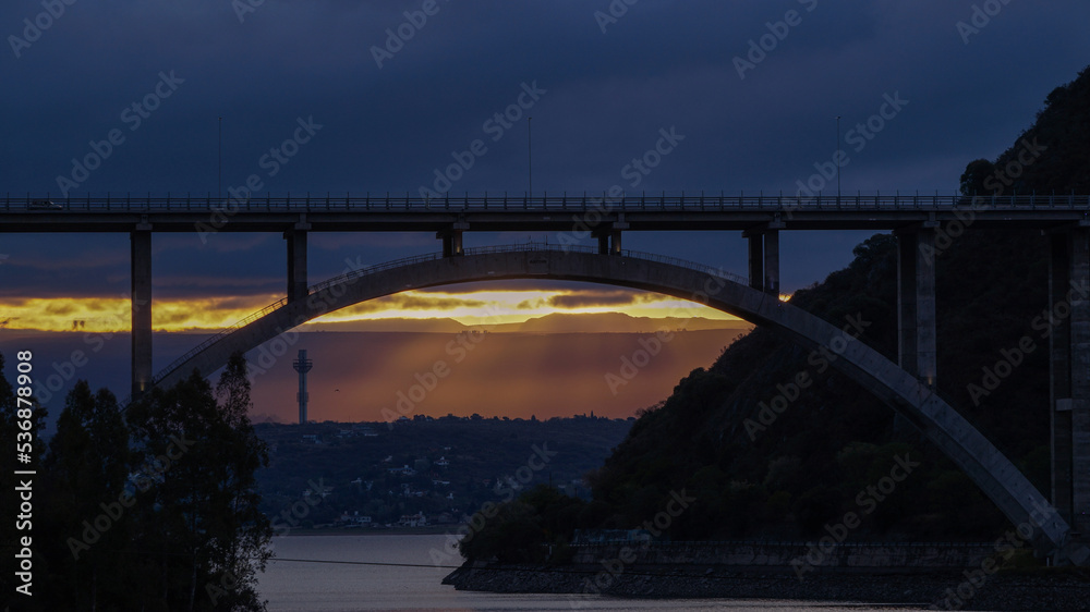 Fototapeta premium Sunset landscape from the San Roque dam, looking to a large bridge and the last minutes of sunlight in Villa Carlos Paz , Cordoba 