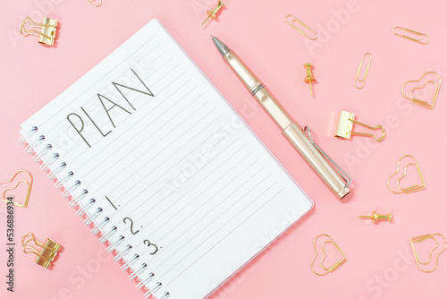 Inscription plan in blank notepad and stationery on pink background copy space.