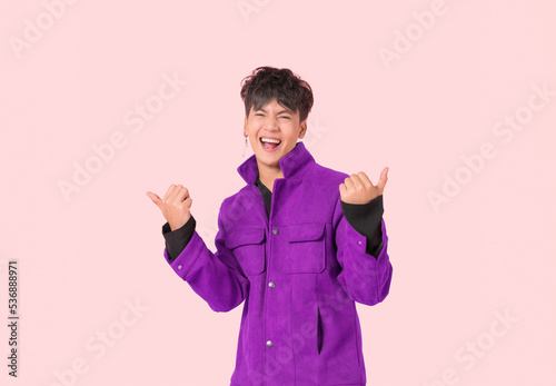 Portrait of happy Asian handsome young man in fashionable jacket clothes standing smiling with thumbs up and look at camera isolated on pink background.