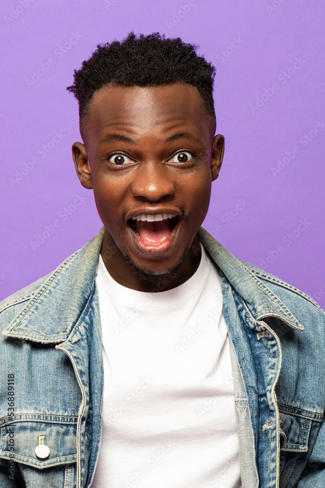Young African man expressing surprised face with popping eyes in isolated purple color studio background Young African man expressing surprised face with popping eyes in isolated purple color studio background