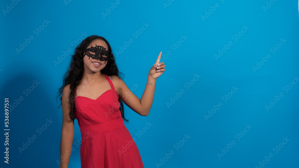 Fototapeta premium Niña con vestido rojo en fondo azul, haciendo poses con antifaz.