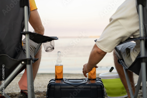 two friends are fishing and drinking beer in the summer at sunset, bottles of beer on the box close-up. leisure and people
