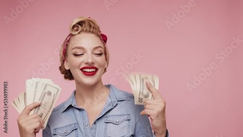 Beautiful blond woman with cash dollars in hands. Caucasian girl hold fan of cash money in dollars banknotes. Girl posing isolated on pink background studio with cash. Pop-art style.