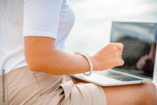 Freelance close up woman hands writing on computer. Well looking middle aged woman typing on laptop keyboard outdoors with beautiful sea view.