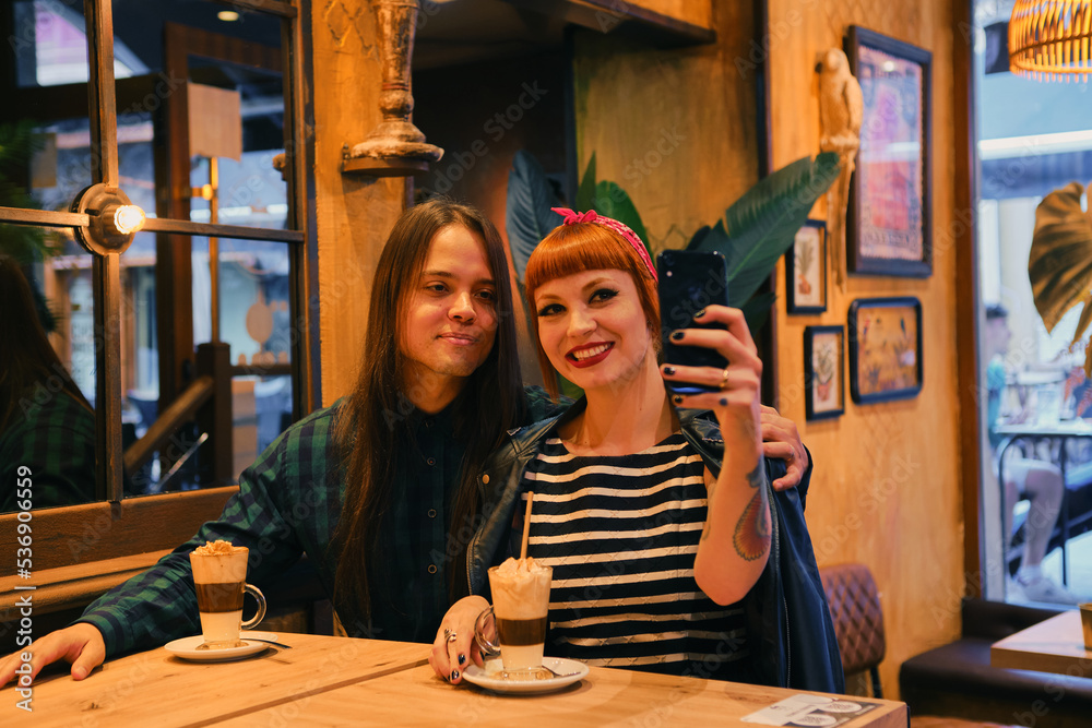 Attractive and stylish couple taking a selfie in a cafe while they are dunking a cappuccino