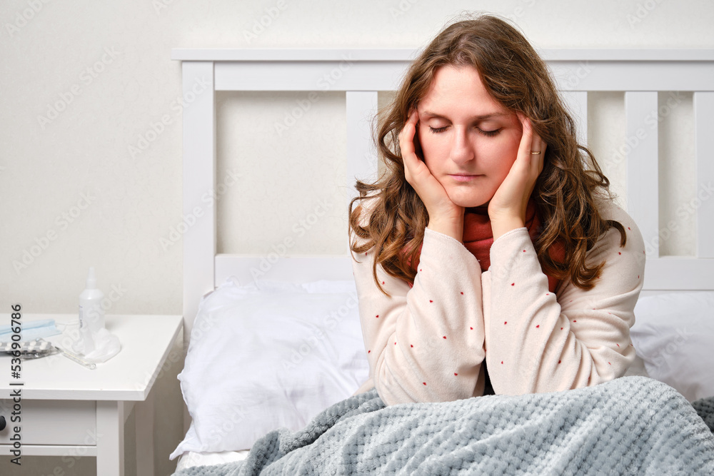 A sick woman is holding on to a sore head, migraine. An adult ill woman is sitting on a home bed in a white bedroomwith a red scarf , female aged 35 years A sick woman is holding on to a sore head, migraine. An adult ill woman is sitting on a home bed in a white bedroomwith a red scarf , female aged 35 years