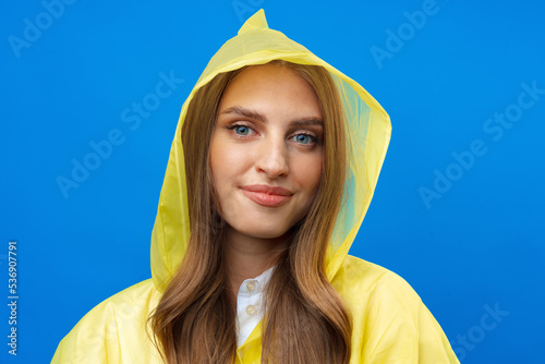 Konstfotografi Young blonde woman wearing yellow raincoat smiling at camera over blue backgroun