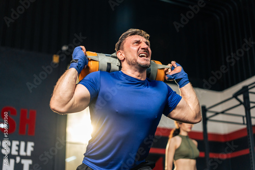 Caucasian sportsman slowly lifting up weight bag or barbell in gym. © Kawee