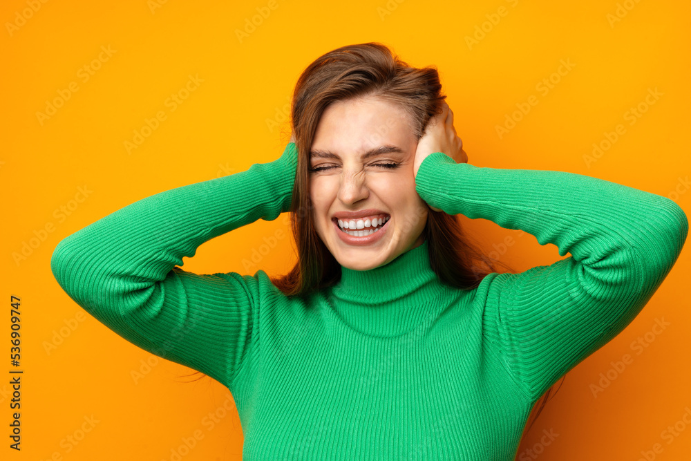 Anxious young woman holding hands on head standing frustrated against yellow background Anxious young woman holding hands on head standing frustrated against yellow background
