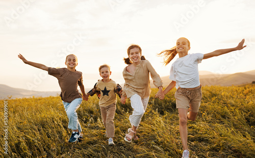 Group of happy joyful school kids boys and girls running with holding hands in field on sunny day