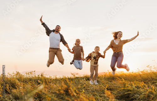 Happy family: mother, father, children son and daughter jumping on sunset