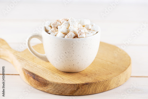 Coffee with marshmallows and cinnamon in a mug on a wooden board.