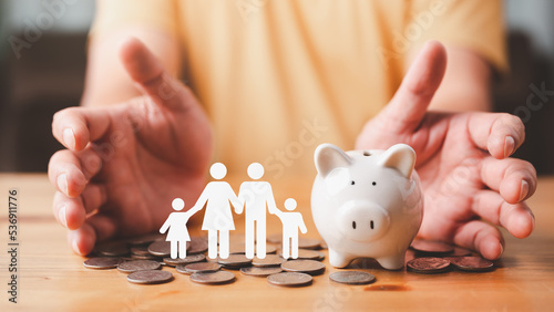 Businessman take a position to protect on the piggybank and paper family in hand, donation, saving, charity, family finance plan concept, fundraising, superannuation, financial crisis concept