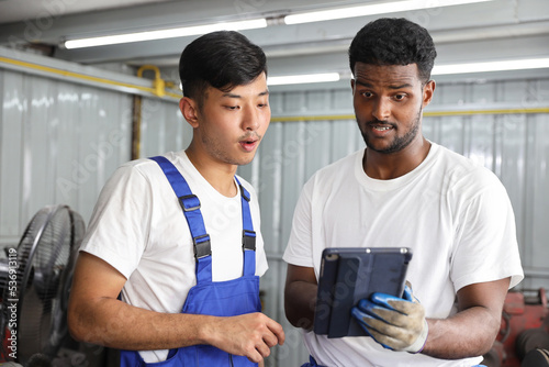 Multiethnic technicain mechanic or worker in half uniform using metal lathe machine operate polishing car disc brake with tablet at garage. Maintenance automotive and inspecting vehicle part concept photo