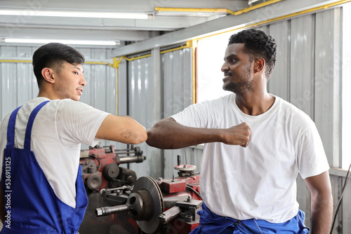 Happy multiethnic technicain mechanic making elbow bump greeting and celebrate successful together completed deal commitment at garage. Maintenance automotive and inspecting vehicle part concept