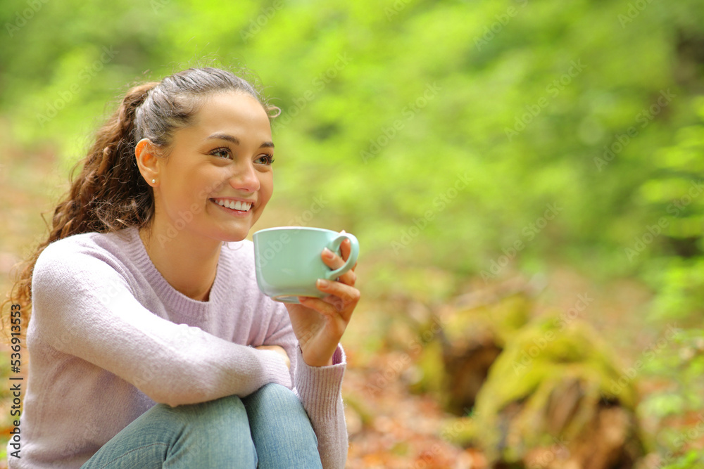 Happy woman in a forest drinking coffee looking away Happy woman in a forest drinking coffee looking away
