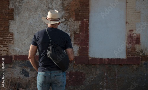 Rear view of adult man holding bag against abandoned building