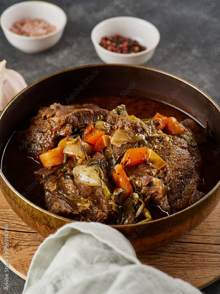 Traditional German braised beef cheeks in brown red wine sauce with herbs as closeup in skillet. - obrazy, fototapety, plakaty 