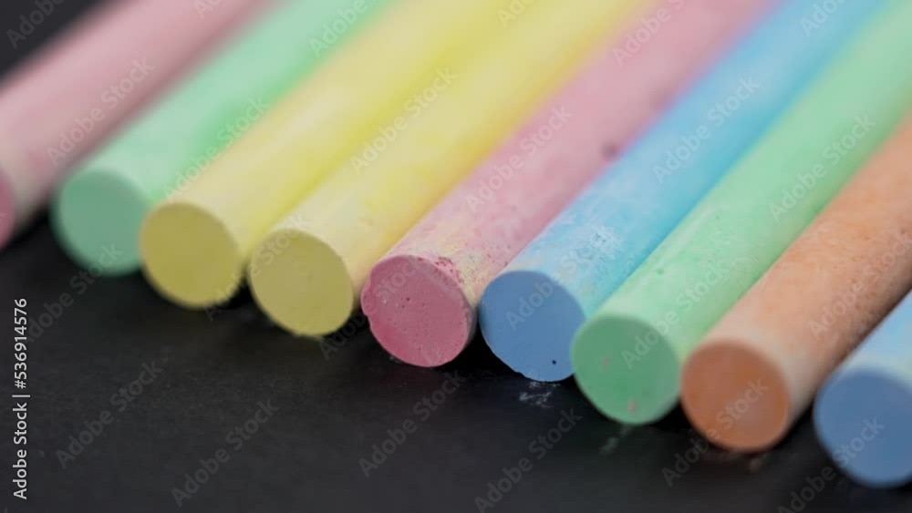 Multicolored set of pastel chalks stacked in a row on a black paper background. Colourful collection. Rotation. Macro shot. Supplies for school and preschool creativity