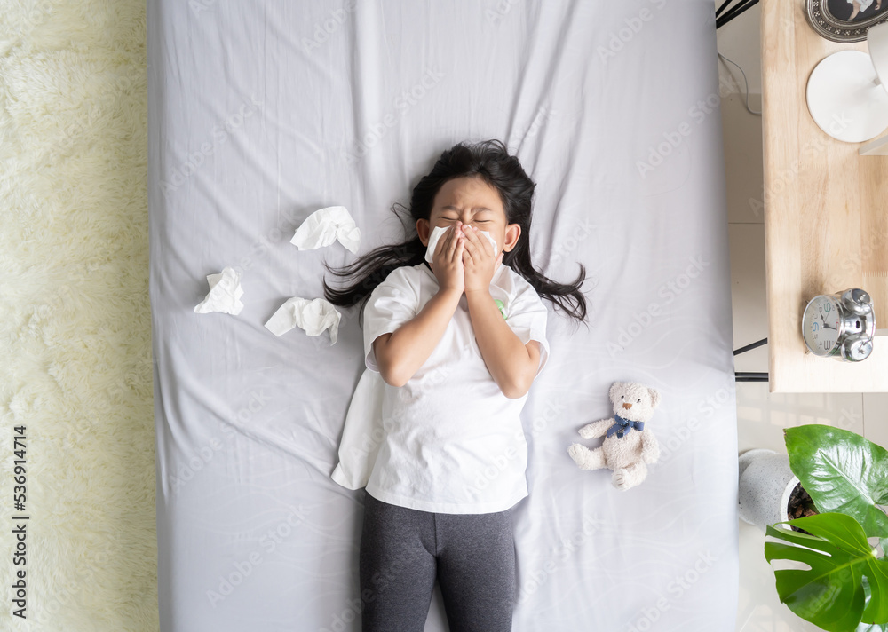 Top view Asian child girl sick with sneezing on the nose and cold cough on tissue paper because weak, Sick child with fever and illness in bed. Top view Asian child girl sick with sneezing on the nose and cold cough on tissue paper because weak, Sick child with fever and illness in bed.