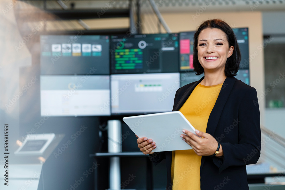 Happy mature businesswoman holding tablet PC in front of computer monitors Happy mature businesswoman holding tablet PC in front of computer monitors