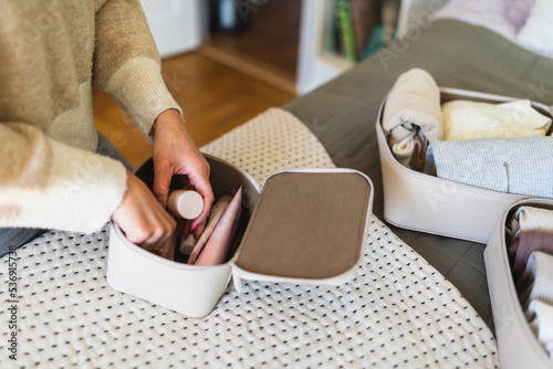 Hands of woman packing beauty product in pouch on bed