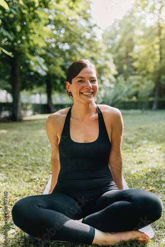 Happy yoga teacher sitting on exercise mat in park photo