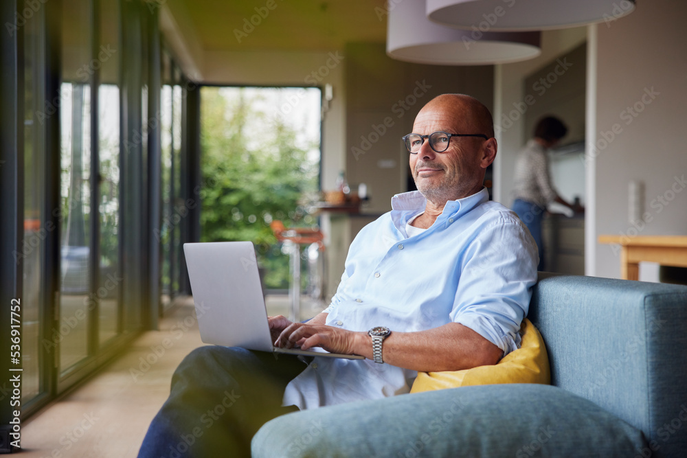 Thoughtful man with laptop sitting on sofa at home Thoughtful man with laptop sitting on sofa at home