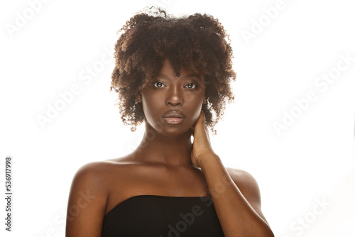Beautiful young lady with dark healthy skin touches her neck.