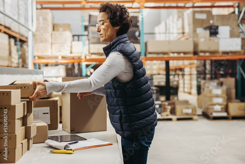 Female warehouse worker packing cardboard boxes while fulfilling online orders