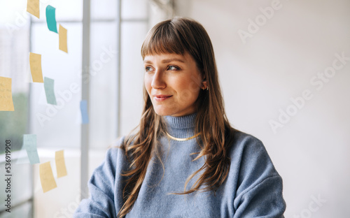 Thoughtful young businesswoman standing next to a glass wall photo