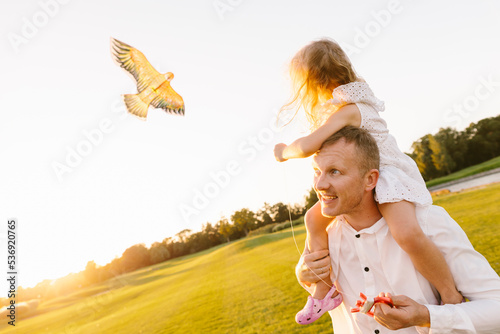 Father carrying daughter on shoulder flying kite in park photo