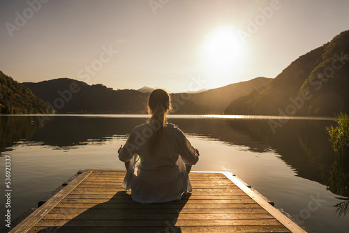 Woman meditating on jetty over lake at vacation photo