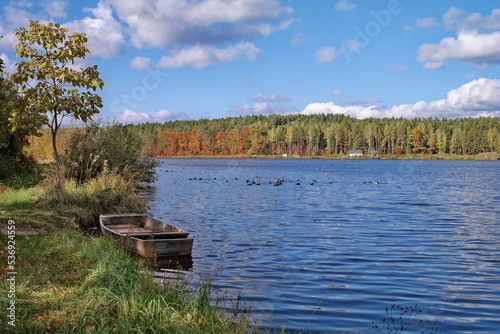 Łódka na tle lasu jesiennego i jeziora w Rudzie Różanieckiej.