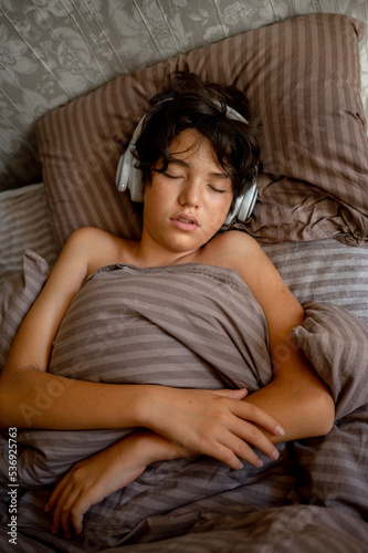 teenage boy sleeps at home on the couch listening to music with headphones