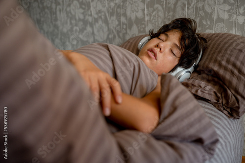 teenage boy sleeps at home on the couch listening to music with headphones © Anastasia Amraeva