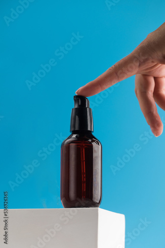 A brown dispenser with a cosmetic product with natural ingredients on a pedestal on a blue background. 