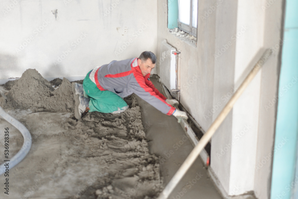 A builder in work clothes is doing his job, leveling the floor, pouring mortar A builder in work clothes is doing his job, leveling the floor, pouring mortar