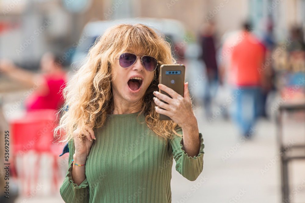 happy mature woman on the street taking a selfie or live video with mobile phone