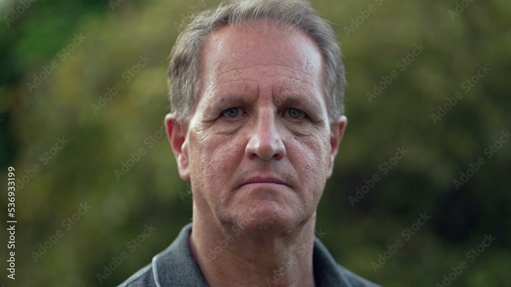 Serious middle aged man standing at park looking at camera. Portrait of an older male person with arms crossed Serious middle aged man standing at park looking at camera. Portrait of an older male person with arms crossed