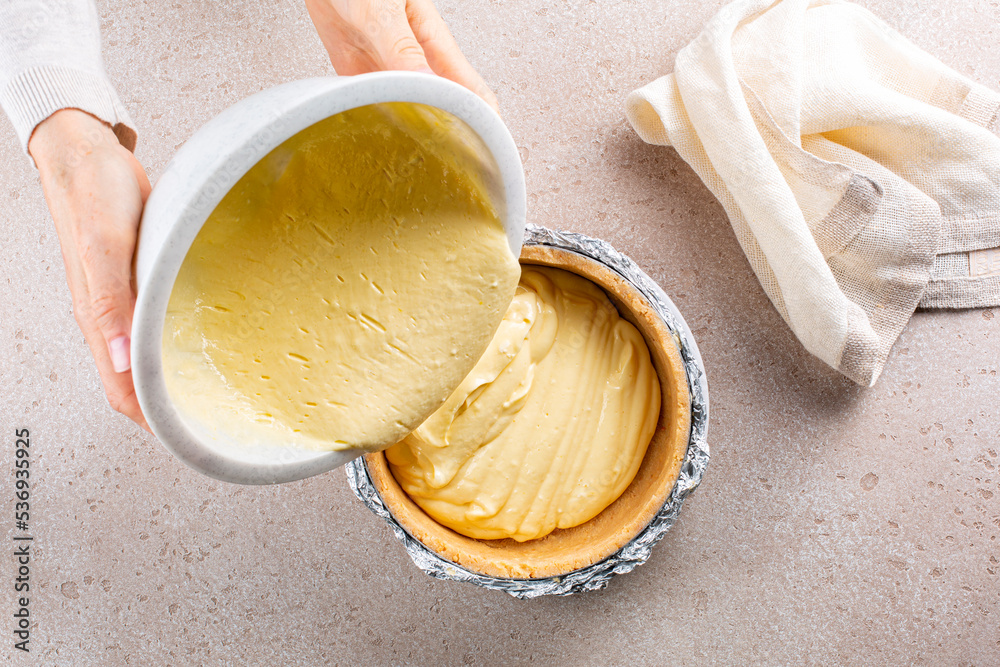 Cooking cheesecake, woman hands pouring a cream cheese into a crust