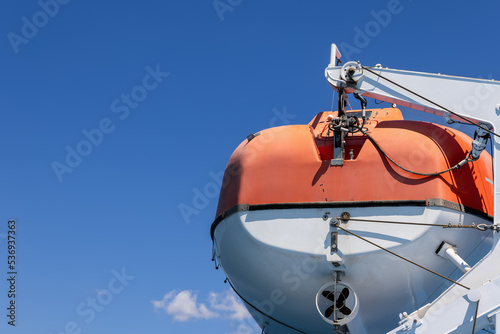 Orange rescue motor boat with which each passenger ferry is equipped, background with clear blue summer morning sky