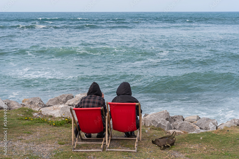 Two friends warm with hoods by the sea on an autumn day
Two friends warm with hoods by the sea on an autumn day