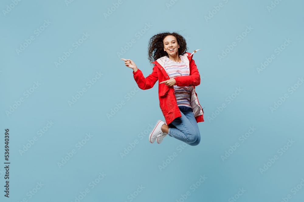 Full body young woman of African American ethnicity wear red jacket jump high point index finger aside on workspace isolated on plain pastel light blue cyan background Wet fall weather season concept Full body young woman of African American ethnicity wear red jacket jump high point index finger aside on workspace isolated on plain pastel light blue cyan background Wet fall weather season concept