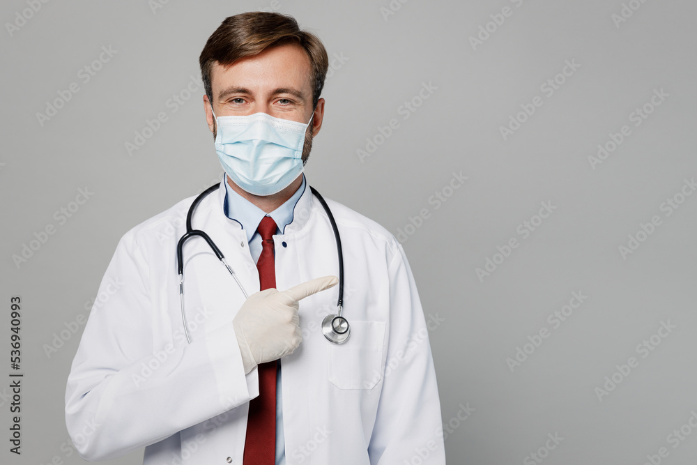 Male doctor man wear white medical gown suit mask gloves work in hospital point index finger aside on workspace area mock up isolated on plain grey color background studio Healthcare medicine concept Male doctor man wear white medical gown suit mask gloves work in hospital point index finger aside on workspace area mock up isolated on plain grey color background studio Healthcare medicine concept