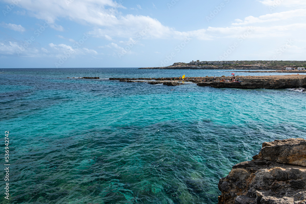 The beautiful Ognina beach in Syracuse with turquoise and green water and a small island in front of it The beautiful Ognina beach in Syracuse with turquoise and green water and a small island in front of it