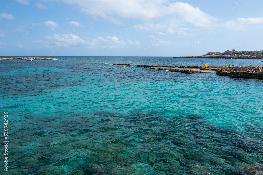 The beautiful Ognina beach in Syracuse with turquoise and green water and a small island in front of it The beautiful Ognina beach in Syracuse with turquoise and green water and a small island in front of it