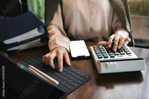 Businesswoman working with tablet and using a calculator to calculate the numbers of static in office. Finance accounting concept.